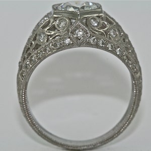 May include: A silver ring with a large, clear, heart-shaped diamond set in a filigree design. The band is also decorated with smaller diamonds.