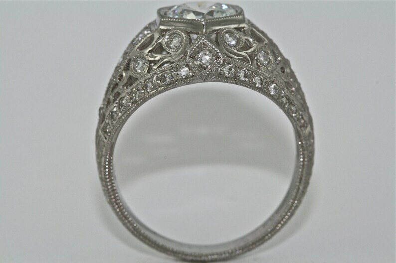 May include: A silver ring with a large, clear, heart-shaped diamond set in a filigree design. The band is also decorated with smaller diamonds.