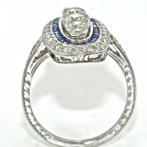 May include: A silver ring with a delicate filigree design and a center stone surrounded by smaller stones. The center stone is surrounded by a halo of blue stones.