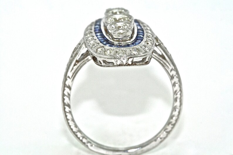 May include: A silver ring with a delicate filigree design and a center stone surrounded by smaller stones. The center stone is surrounded by a halo of blue stones.