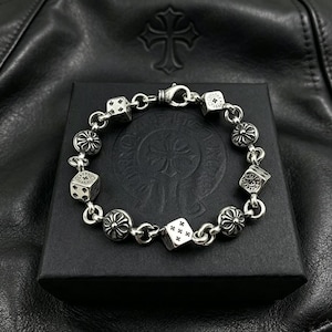 Pode incluir: Uma pulseira de corrente de prata com berloques alternados em forma de dados e medalhões circulares de estilo floral. Os dados são marcados com pequenos símbolos de cruz em vez de pontos tradicionais. A pulseira inclui um fecho de mosquetão.
