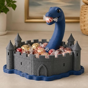 May include: A dark blue dinosaur figure with a long neck emerging from a gray castle-shaped bowl. The dinosaur holds a round, red and white striped candy in its mouth. The castle base is surrounded by a blue wavy border and filled with candies.