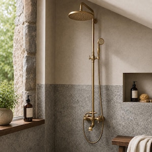 Puede incluir: Un sistema de ducha montado en la pared con acabado en latón cepillado que incluye un cabezal de ducha circular grande, una ducha de mano flexible con manguera y un grifo inferior con dos mandos en cruz para regular el agua.