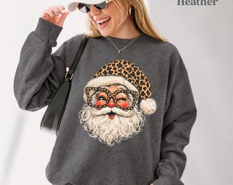 May include: A dark heather gray crewneck sweatshirt featuring a graphic of Santa Claus wearing a leopard print hat and matching leopard print glasses. The text "Dark Heather" is printed in the upper right corner of the image.