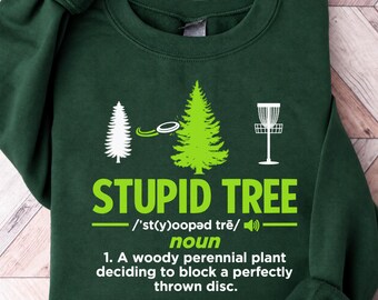 May include: A dark green crewneck sweatshirt featuring a white and lime green graphic. The design shows a disc golf disc flying toward a tree and a basket, with the text STUPID TREE, phonetic spelling, and a dictionary-style definition.