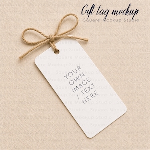 May include: A rectangular white gift tag with rounded corners, featuring a brown twine bow tied through a hole at the top. The tag displays the black text YOUR OWN IMAGE / TEXT HERE. The top right corner shows the text Gift tag mockup Square Mockup Studio.