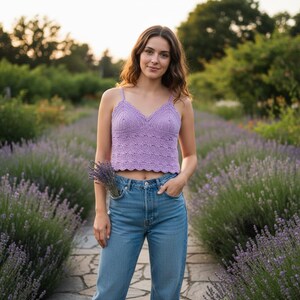 May include: A lavender crochet crop top featuring a V-neckline with a scalloped edge and thin spaghetti straps, paired with light blue denim jeans. The top has a textured, intricate knit pattern throughout the bodice and a cropped hemline.