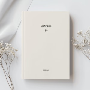 May include: A cream-coloured hardcover book with black text on the front cover. The text reads CHAPTER 30 at the top and EMILY at the bottom. The book is positioned vertically with a clean, solid-coloured surface and delicate dried white flowers.