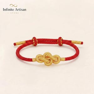 May include: A red cord bracelet featuring a central gold-colored knot ornament. The bracelet includes two adjustable sliding knots and gold-colored metal tips at each end of the cord. The text Infinite Artisan STORE is visible above.
