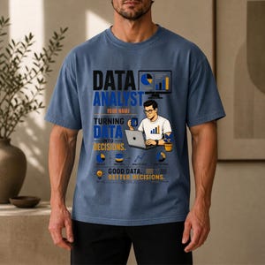 Puede incluir: Una camiseta azul de manga corta con un estampado gráfico que incluye el texto DATA ANALYST, YOUR NAME, TURNING DATA INTO DECISIONS y GOOD DATA, BETTER DECISIONS. El diseño muestra a una persona usando un portátil, gráficos e iconos.