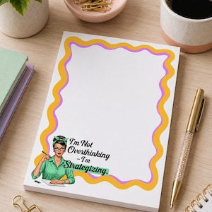 May include: A white notepad featuring a wavy yellow and purple border. At the bottom left, an illustration shows a person with dark hair in a green headband and shirt, wearing glasses, holding a pen. The text reads: I'm Not Overthinking - I'm Strategizing.