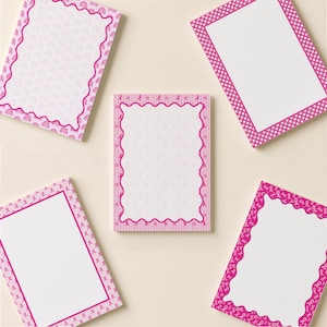 May include: Five rectangular notepads with white centers and pink decorative borders. The borders feature various patterns including pink polka dots, wavy lines, and small pink ribbon icons, arranged in a circular layout on a light background.