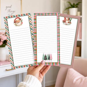 May include: Three rectangular paper notepads with lined pages. The left pad has a Santa Claus illustration and a star border. The center pad features a plaid border and Christmas tree graphics. The right pad has a red plaid border and Joy to the world text.