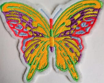 May include: Embroidered butterfly patch with a white border. The butterfly features yellow, orange, purple, red, and green details. The text "We invite you to try our" is printed below the patch.