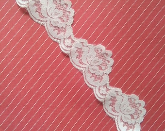 May include: White lace trim with a delicate floral pattern against a red striped background.