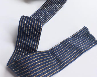 May include: Navy blue ribbon with gold metallic stripes. The ribbon is rolled up and partially unraveled, showcasing its texture and design. This decorative ribbon is suitable for various craft projects and embellishments.