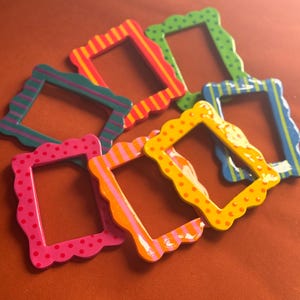 May include: A collection of six rectangular picture frames with scalloped edges, featuring various patterns including polka dots and stripes in vibrant colours such as pink, orange, yellow, green, blue, and teal, arranged in an overlapping cluster.