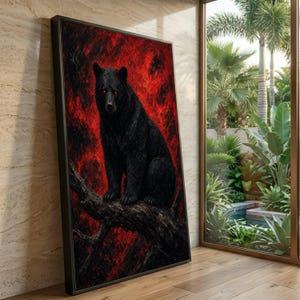 May include: A framed vertical wall art piece featuring a black bear with glowing red eyes perched on a dark tree branch against a textured, vibrant red background. The artwork is enclosed in a thin black frame and displayed on a light-colored floor.