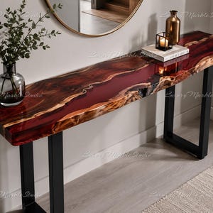 May include: A console table featuring a live-edge wood slab with a deep red resin river inlay, supported by black metal legs. The surface is polished and glossy, displaying natural wood grain patterns. The table is rectangular in shape.