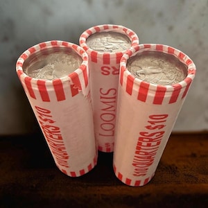 May include: Three cylindrical coin rolls containing US quarters, each wrapped in white paper with red stripes. The paper is printed with the text $10 QUARTERS $10 and LOOMIS. The top of each roll reveals the metallic surface of a quarter coin.