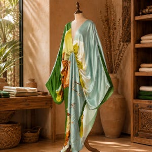 May include: A floor-length satin kaftan dress featuring a V-neckline and wide, flowing sleeves. The garment displays a vibrant botanical print with large abstract floral patterns in shades of sage green, lime yellow, and deep forest green.