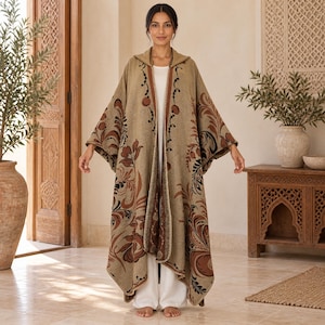 May include: A hooded beige cloak featuring a brown and black floral pattern. The garment has an open front design with a brown trim along the edges and a white base layer underneath. The fabric displays large, sweeping botanical motifs throughout.