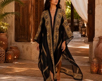 May include: A long, flowing black kimono-style robe featuring intricate gold and brown paisley patterns along the front panels, sleeves, and hem. The garment has an open front design, wide sleeves, and a lightweight, sheer fabric construction.