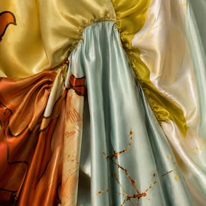 May include: A smooth, lustrous fabric garment featuring gathered sections and a multi-colored print. The material displays a palette of golden yellow, soft mint green, and deep burnt orange with abstract, thin brown line patterns.