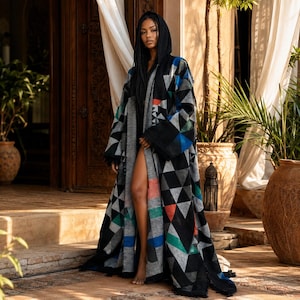 May include: A long, hooded open-front cloak featuring a geometric pattern of black, grey, white, blue, green, and orange triangles. The garment has wide sleeves and a textured fabric construction that drapes to the floor, creating a layered appearance.