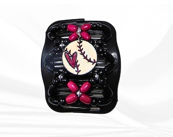 Può includere: Un pettine per capelli nero con un ciondolo centrale circolare raffigurante un baseball e un cuore rosso. Il pettine è decorato con perline nere e magenta disposte a motivi floreali, collegate da cordini elastici flessibili.