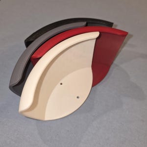 May include: A set of three nested corner shelves in white, red, and black. Each shelf features a curved front edge and two small circular mounting holes on the flat back panel. The shelves are stacked together, showing their distinct colors and shapes.