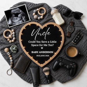 May include: A heart-shaped light-up letter board with the text Uncle Could You Save a Little Space for Me Too? BABY ANDERSON DUE JUNE 2026, surrounded by an ultrasound, baby bottle, wooden teethers, sunglasses, watch, car key, coffee, controller, and grooming items.