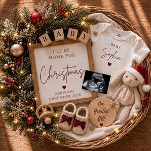 May include: A wicker basket containing a white baby onesie with the text Baby Sophia, a wooden sign reading I'll be home for Christmas arriving December 2026, a sonogram, a plush rabbit in a Santa hat, knit booties with bows, and a wooden pacifier.
