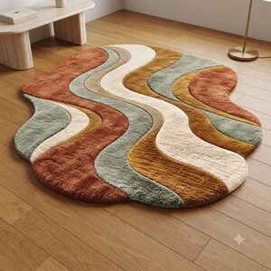 Pode incluir: Um tapete de formato orgânico irregular com um padrão ondulado multicolorido. O design consiste em faixas curvas e fluidas em tons de terracota, creme, amarelo mostarda e verde sálvia, criando uma aparência texturizada e em camadas.