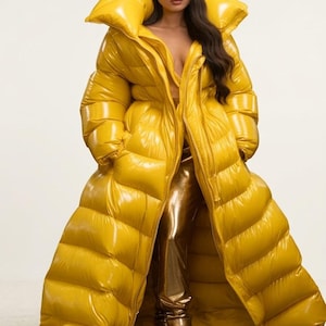 Peut inclure: Un long manteau doudoune jaune moutarde brillant doté d'un col haut surdimensionné, de canaux matelassés horizontaux et d'une fermeture éclair intégrale. Le manteau est porté sur un pantalon doré métallisé et des bottes dorées assorties.
