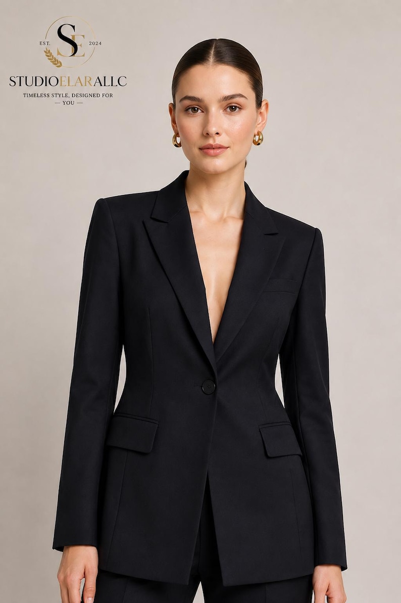 May include: A tailored black blazer featuring a single-button closure, notched lapels, and two front flap pockets. The garment is structured with long sleeves and a clean, solid finish. The logo text STUDIOELARALLC EST. 2024 is visible.