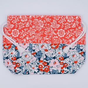 May include: A rectangular drawstring pouch featuring a two-tone floral pattern. The top section displays a vibrant coral-orange background with white botanical motifs, while the bottom section showcases a dense floral print in navy, coral, and pink.