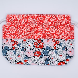 May include: A rectangular drawstring pouch featuring two distinct floral patterns. The top section displays a vibrant red fabric with a white botanical print, while the bottom section showcases a dense floral design in red, pink, and dark blue.