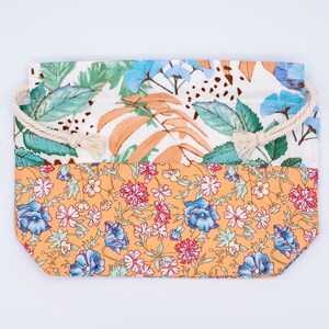 May include: A rectangular fabric pouch featuring a two-tone design. The top section displays a white background with green leaves and orange fronds. The bottom section features an orange background with a dense floral pattern of blue and pink flowers.