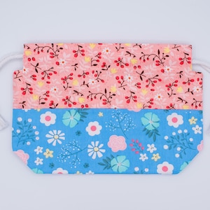 May include: A rectangular drawstring pouch featuring a two-tone design. The top section is a light coral fabric with a pattern of small white flowers and dark red berries. The bottom section is a bright blue fabric with white and pink flowers.