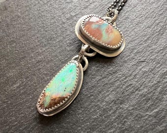 May include: A silver chain necklace with two pendants. The top pendant is a heart-shaped opal with brown and pink hues. The bottom pendant is a teardrop-shaped opal with green and blue hues.