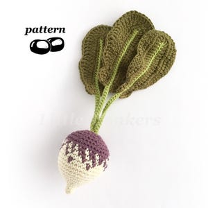 May include: A crochet turnip toy featuring a round root with a cream-coloured bottom and a purple top with a zigzag pattern. The vegetable has several large, textured dark green leaves attached to long, light green stems. The text pattern is visible.