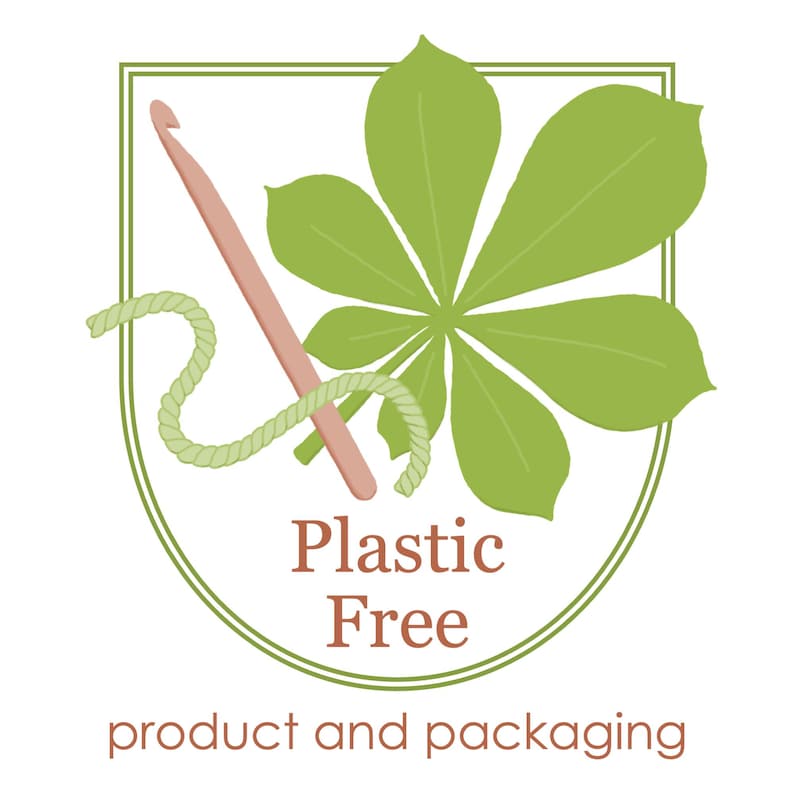 May include: A shield-shaped logo featuring a green seven-lobed leaf, a pink crochet hook, and a length of light green yarn. The text reads Plastic Free in brown, with product and packaging written below in smaller brown lowercase letters.