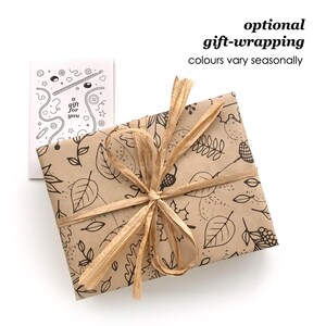 May include: A rectangular gift wrapped in brown paper with a black line-art pattern of leaves and acorns, tied with a tan raffia ribbon. Beside it is a white card with black line-art illustrations and the text 'a gift for you'.