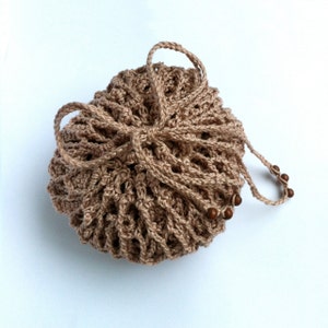 May include: A round, light brown crocheted drawstring pouch featuring an open-work lattice pattern. The bag is cinched at the top with matching crocheted cords that form a bow, and the ends of the cords are decorated with small, round, dark brown wooden beads.