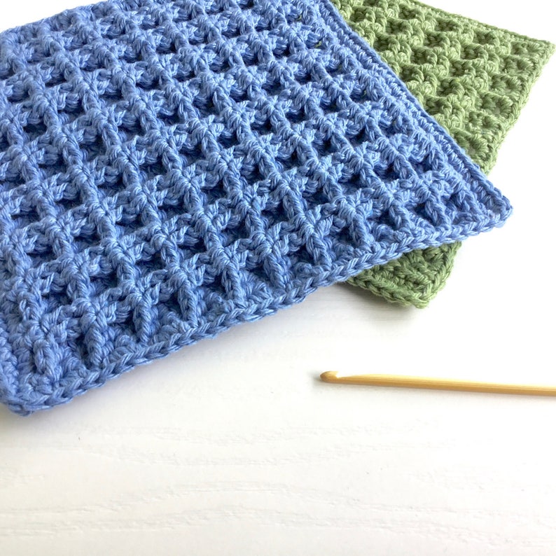 Two crocheted dishcloths, one in blue yarn, one in green yarn. The square dishcloths are crocheted with a stitch that gives them a waffle-like appearance and texture. There is a hanging loop in one corner of the dishcloths.