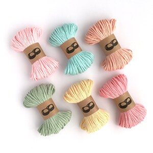 May include: Six bundles of twisted cord arranged in two rows. The colors include light pink, mint green, peach, sage green, pale yellow, and rose pink. Each bundle is secured with a brown paper band featuring a black icon of two rounded shapes.