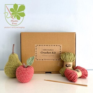 May include: A Little Conkers Crochet Kit in a brown cardboard box with a label, featuring a crocheted green pear, a red apple with a green leaf, two skeins of yarn in green and red, and a wooden crochet hook, with a plastic-free logo.