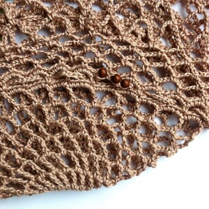 May include: A light brown crocheted net bag featuring an openwork diamond pattern. The textile is constructed from thin yarn and includes three small, round, dark brown wooden beads threaded onto one of the horizontal strands of the mesh.