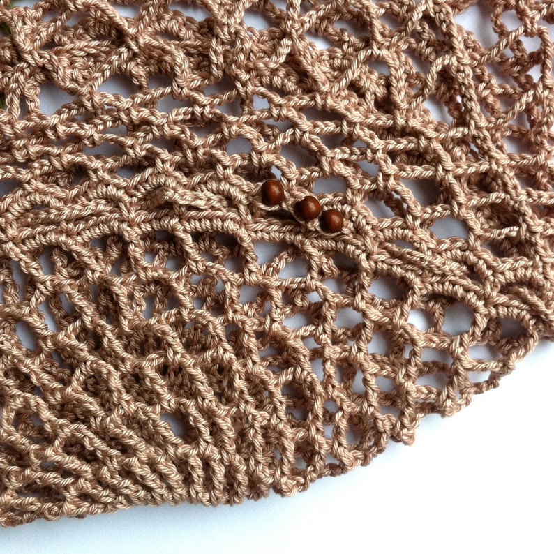 May include: A light brown crocheted net bag featuring an openwork diamond pattern. The textile is constructed from thin yarn and includes three small, round, dark brown wooden beads threaded onto one of the horizontal strands of the mesh.